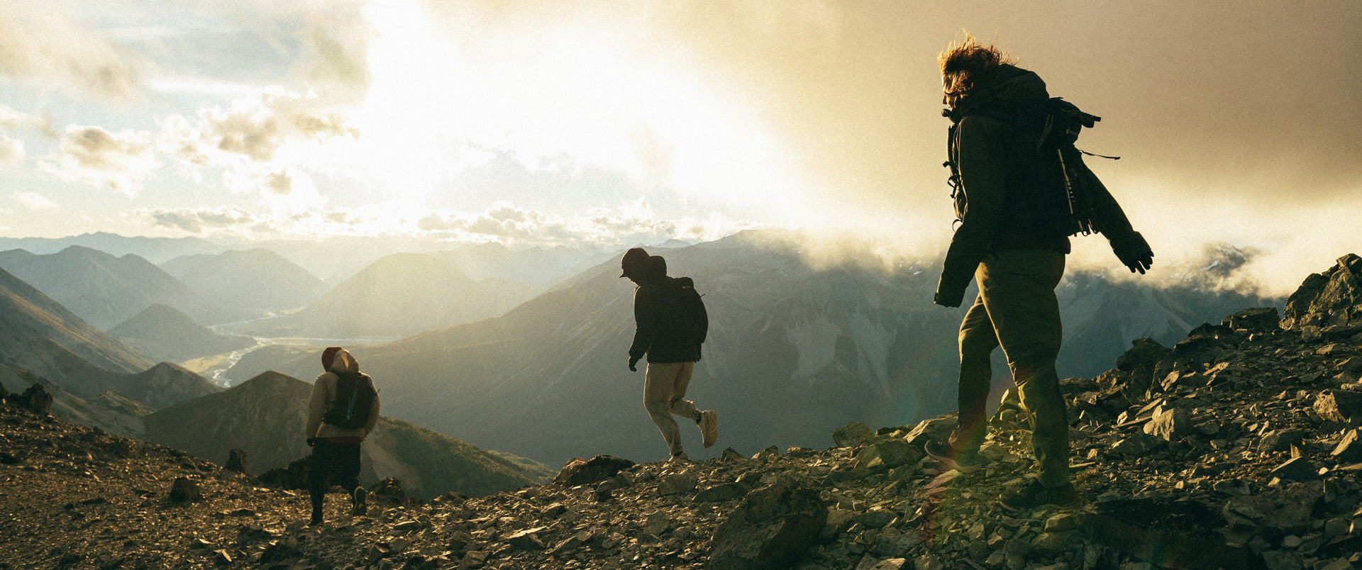Three people hiking on a mountain with a scenic view of mountains and sky.
