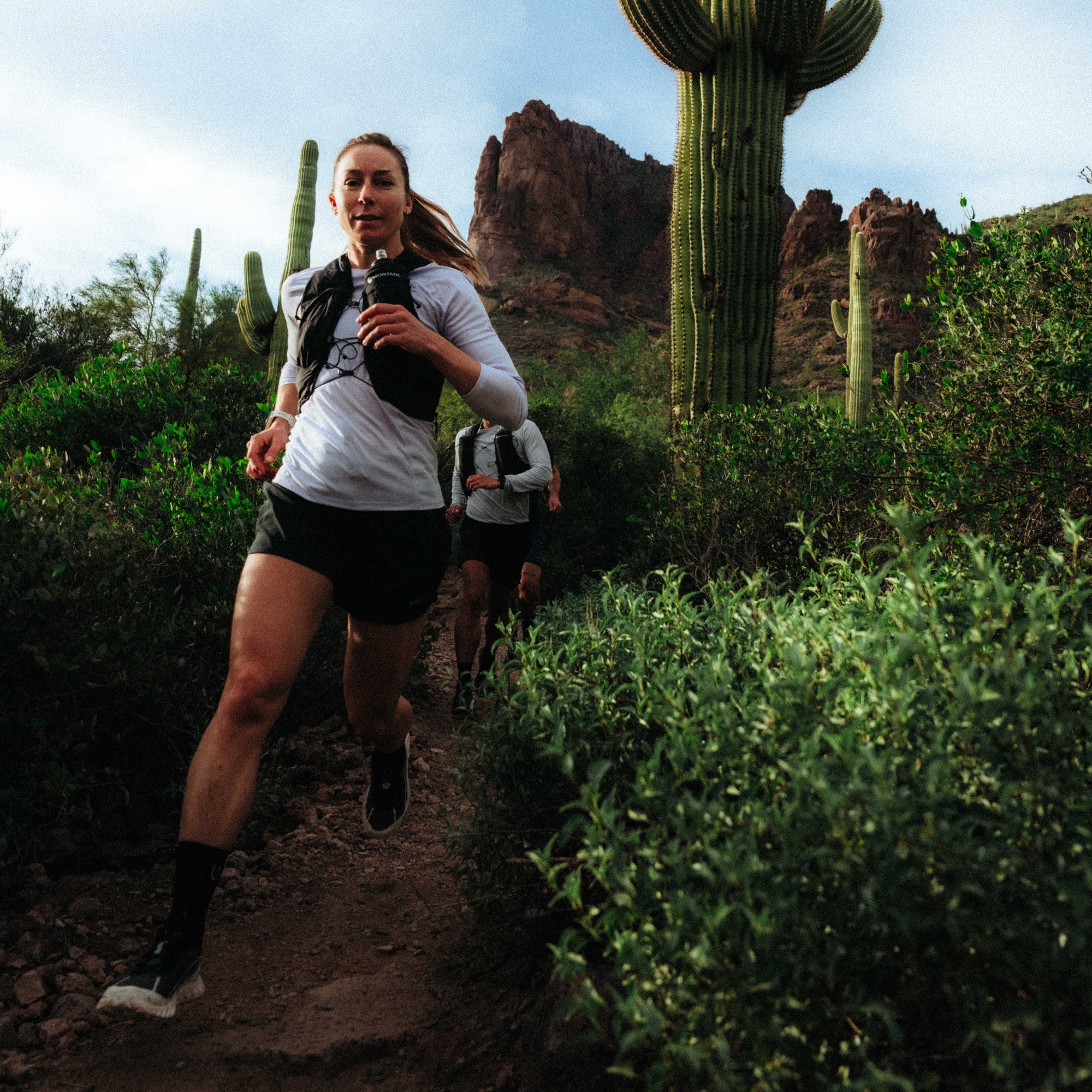 Woman trail running in desert landscape with saguaro cacti and mountains